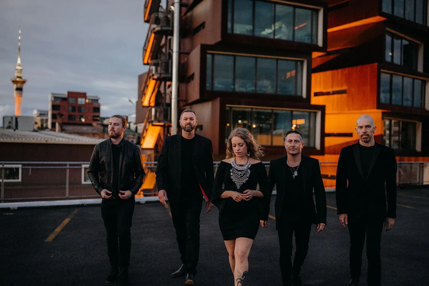Hands Off, Auckland's five-piece covers band, walking a city rooftop at dusk with the Sky Tower behind them
