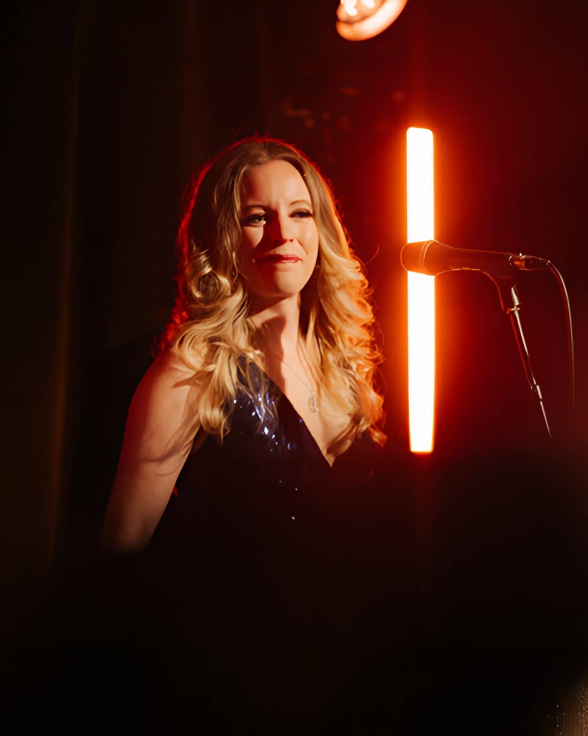The singer smiling at the mic, a red light bar behind