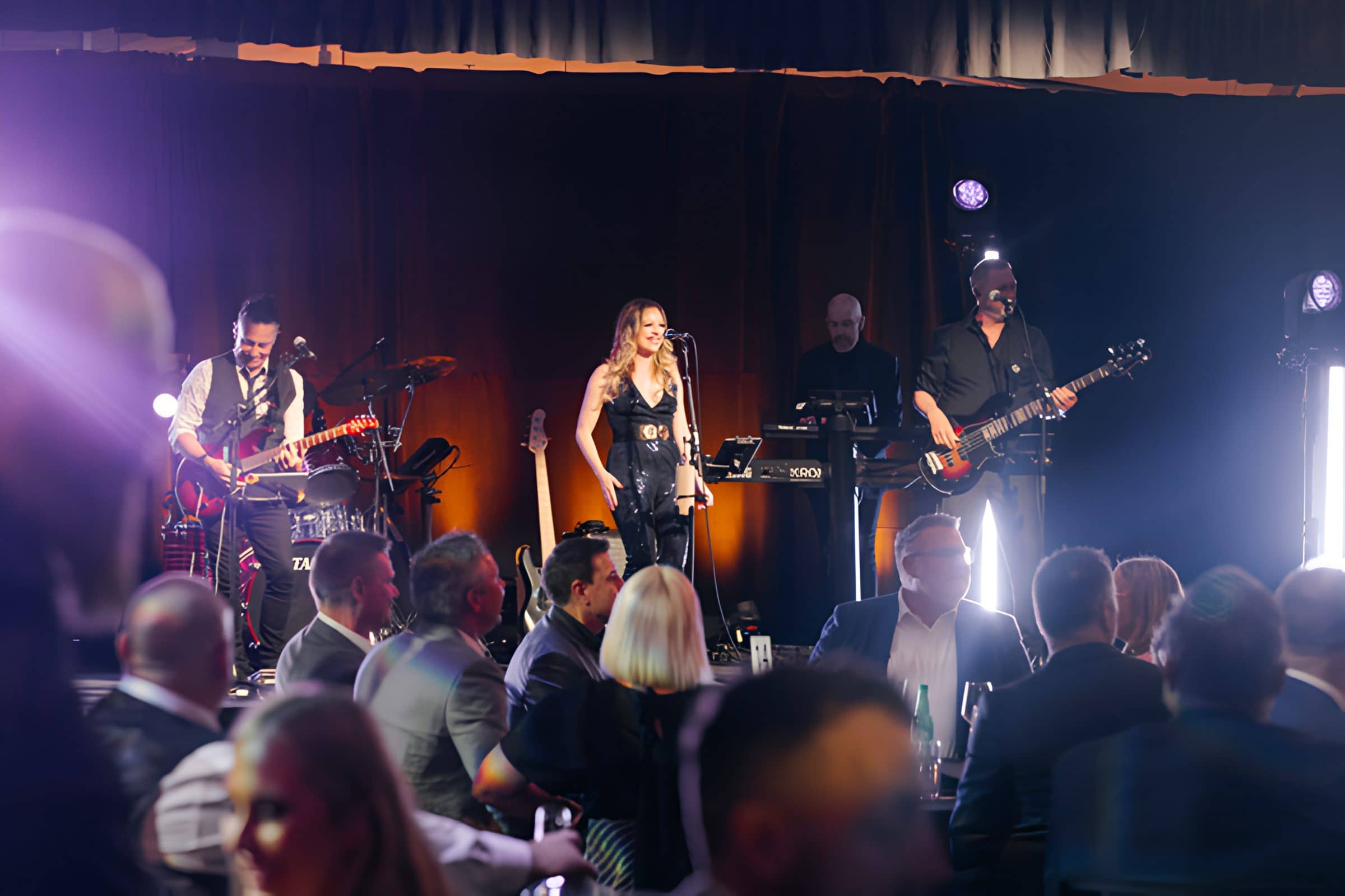 Hands Off mid-set at an awards dinner, stage light flaring across the room