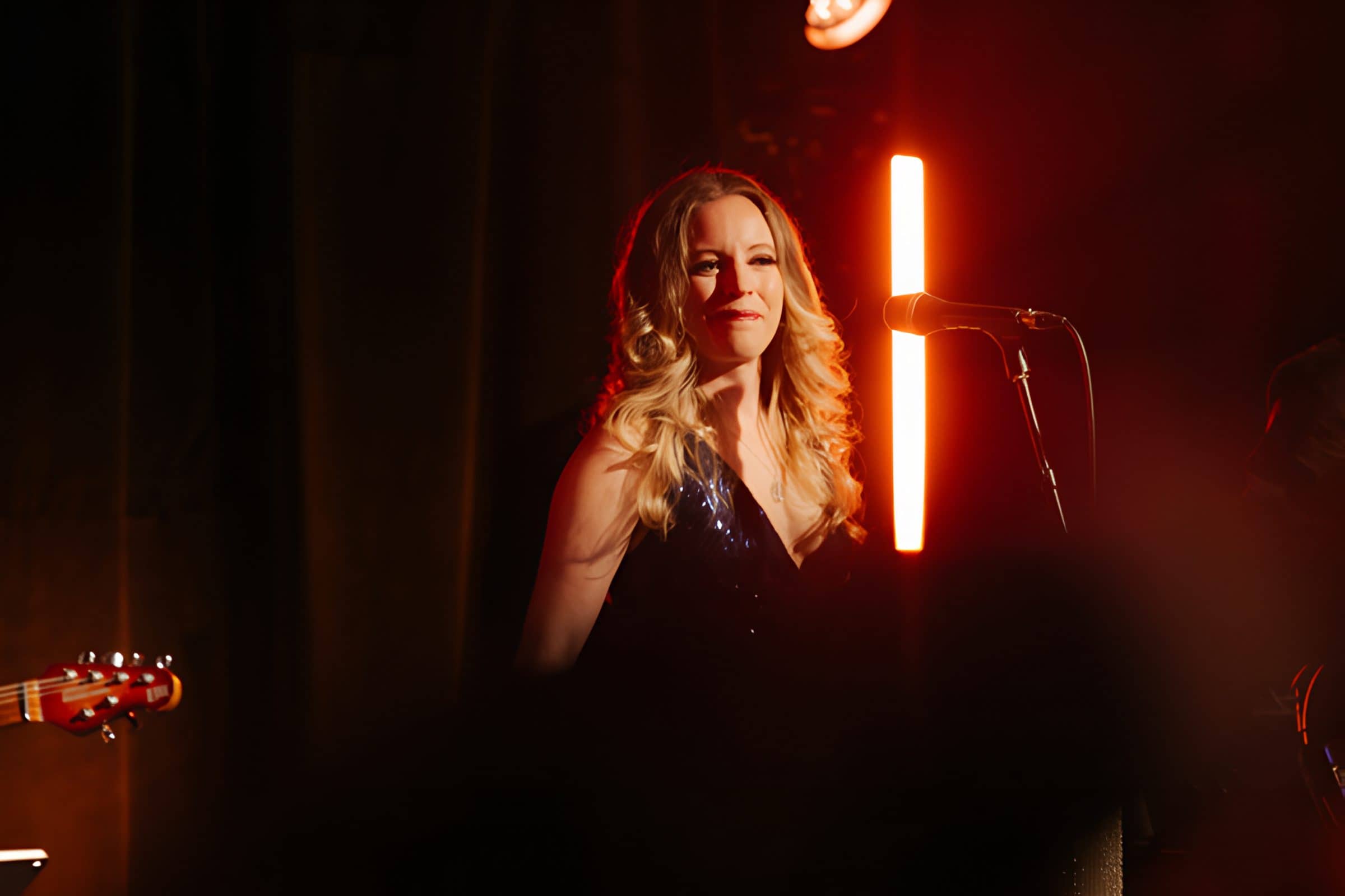 The singer smiling at the mic under red stage light